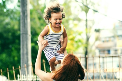 Parent lifting a laughing toddler in the air outdoors