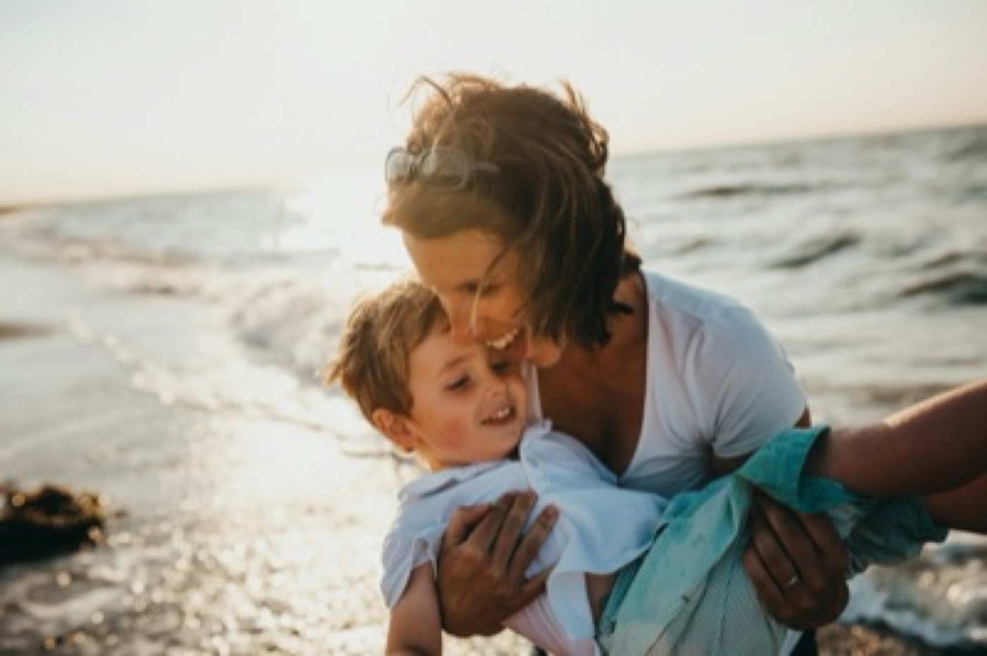 Mother hugging her young child at the beach, golden hour light